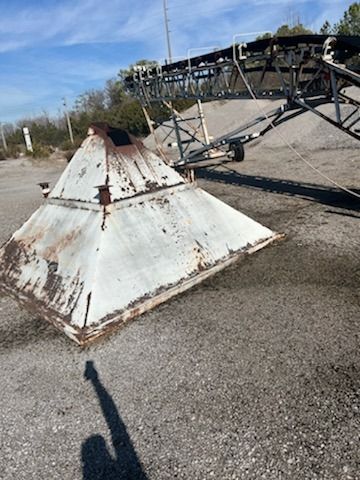 A large metal pyramid is sitting on top of a gravel road.