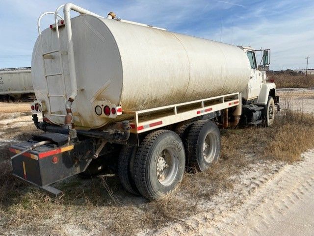 A white tanker truck is parked on the side of a dirt road.