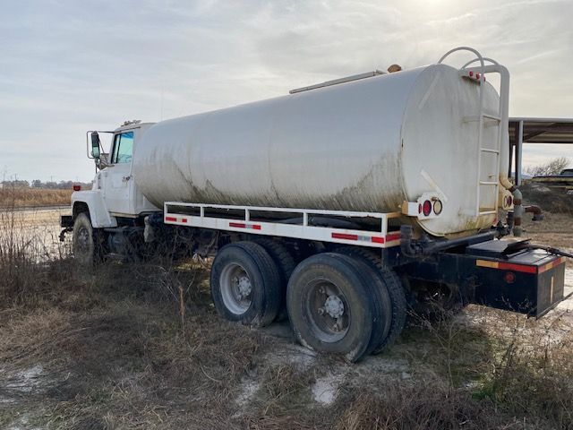A white tanker truck is parked in a field.