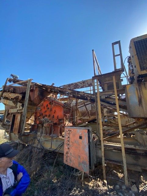 A man in a blue jacket is sitting in front of a large machine.