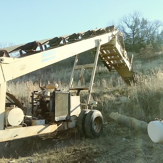 A tractor with a conveyor belt is parked in a field