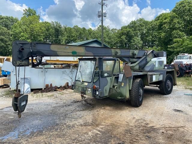 A military truck with a crane attached to it is parked in a dirt lot.