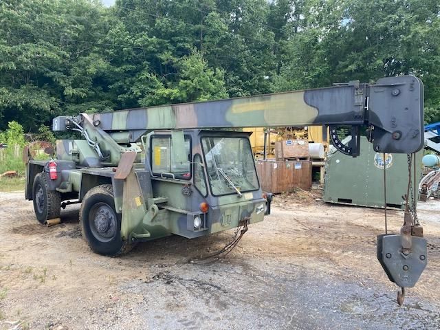 A military truck with a crane attached to it is parked in a dirt lot.