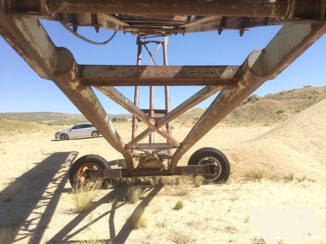 A car is parked behind a rusty metal structure in the desert