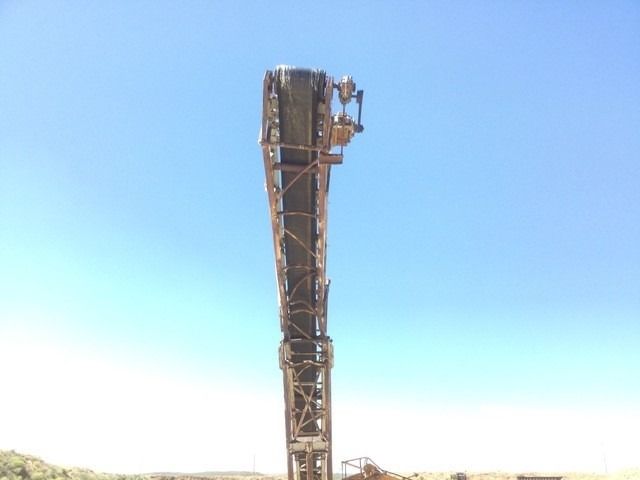 A large tower with a conveyor belt attached to it against a blue sky.