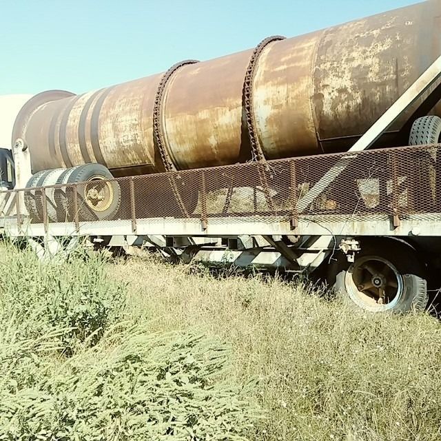 A large rusty pipe is on the back of a truck