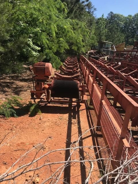 A row of conveyor belts in a field with trees in the background