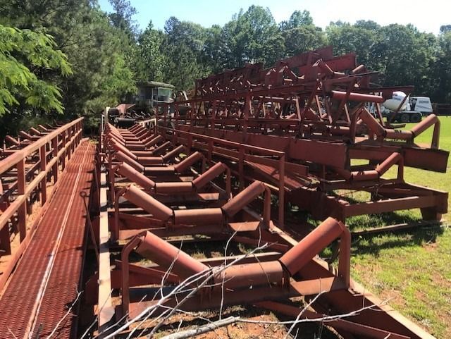 A row of conveyor belts in a field with trees in the background