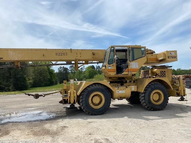 A large yellow crane is parked in a dirt lot.