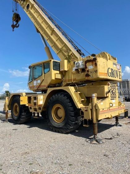 A yellow grove crane is parked in a gravel lot