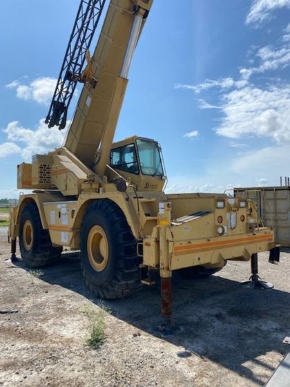 A large yellow crane is parked in a dirt field