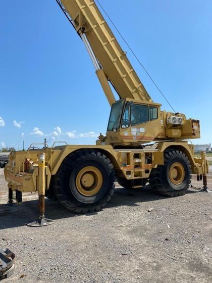 A large yellow crane is parked in a dirt field