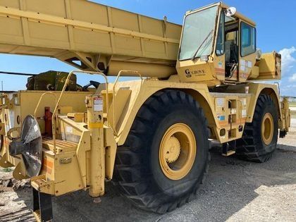 A large yellow crane is parked on a dirt road.