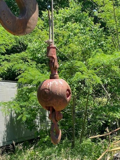 A crane hook is hanging from a rope in the woods.