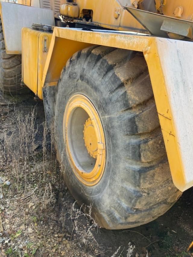 A yellow tractor with a large tire is parked in the dirt.
