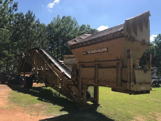A large machine with a conveyor belt is parked in a grassy field.