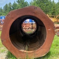 A large rusty pipe is sitting in the grass in a field.