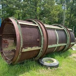 A large rusty metal pipe is sitting in the grass next to a tire.