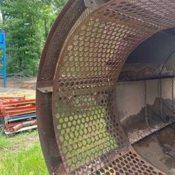 A large metal pipe with holes in it is sitting in the grass.