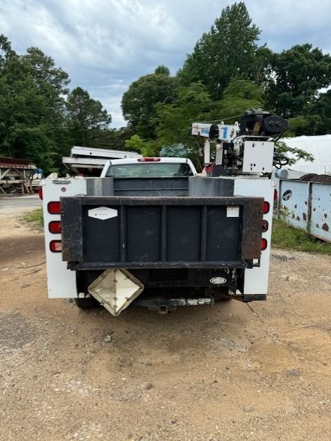 A white truck with a black bed is parked in a dirt lot