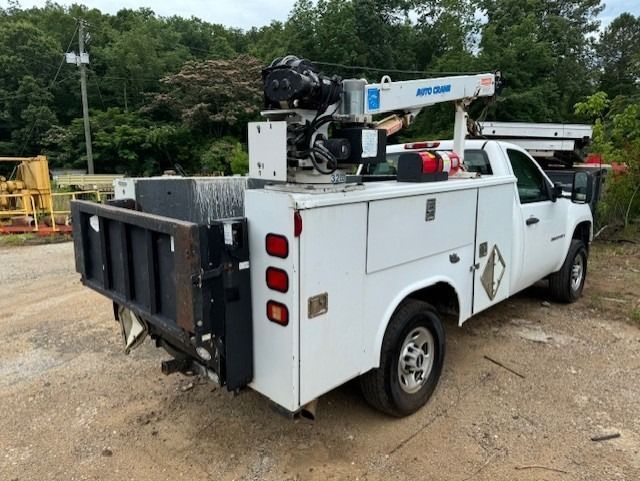 A white utility truck with a crane on the back is parked in a dirt lot.