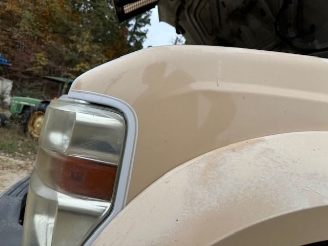 A close up of the front of a truck with a tractor in the background.