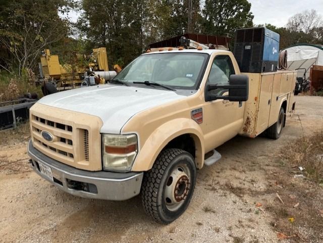 A tan and white utility truck is parked in a dirt lot.