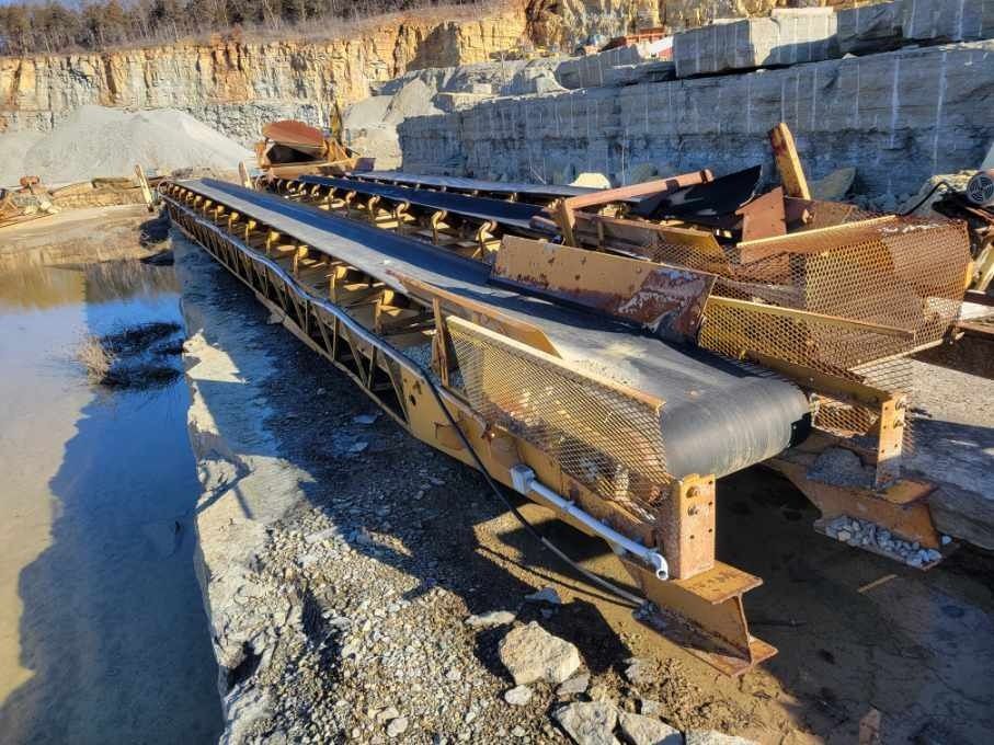 A conveyor belt is sitting next to a body of water in a quarry.
