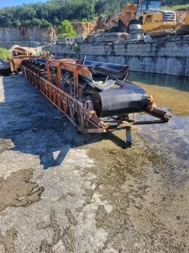 A conveyor belt is sitting on top of a dirt field next to a body of water.