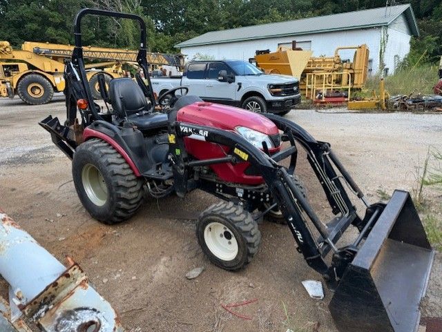 A red tractor with a black bucket is parked in a dirt lot.