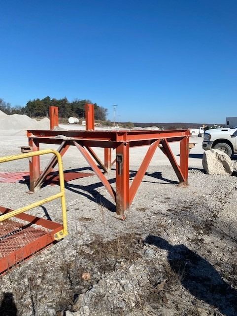 A red metal structure with a yellow railing in a dirt field