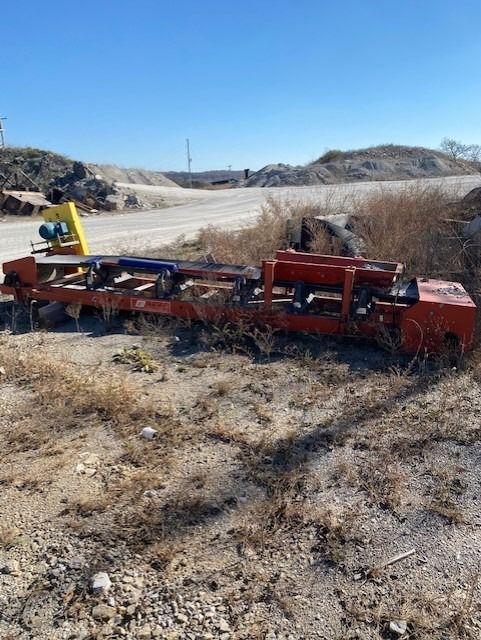 A large red machine is sitting in the middle of a dirt field.