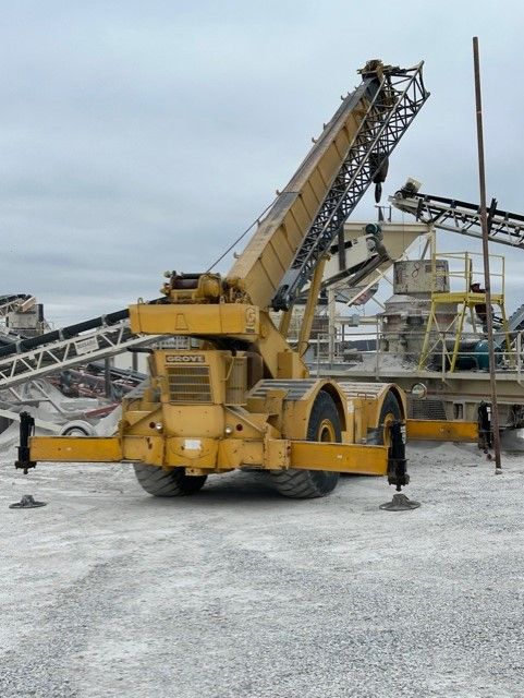 A large yellow crane is parked in a gravel area