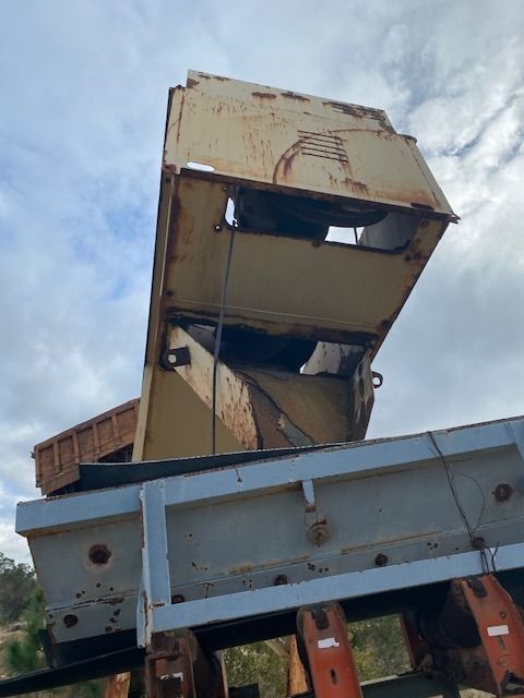An old rusty truck with the hood open is sitting on top of a conveyor belt.