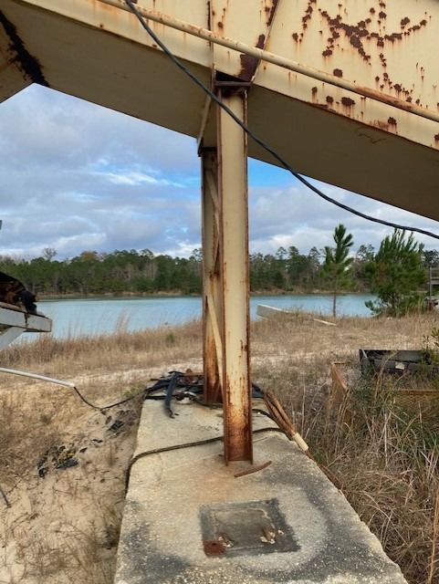A rusty metal structure in a field with a lake in the background