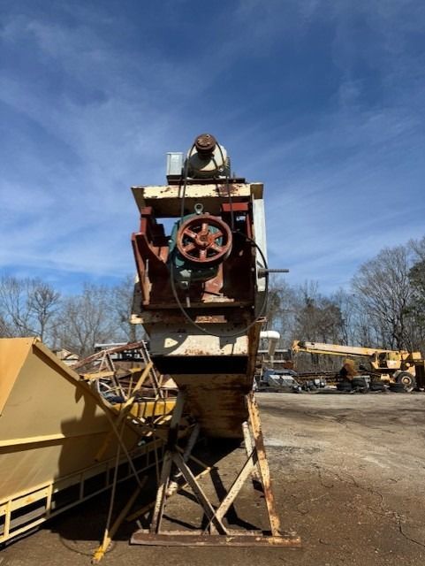 A large machine is sitting in a parking lot with trees in the background