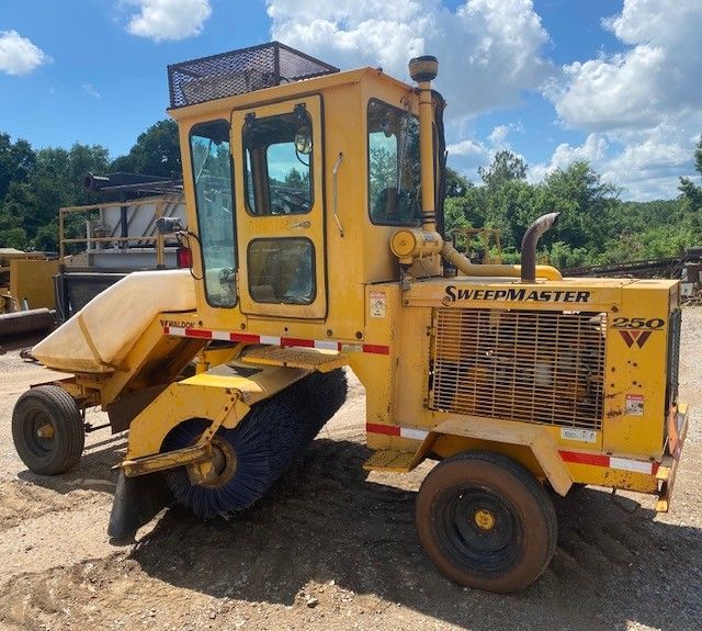 A yellow sheepmaster tractor is parked in a dirt lot