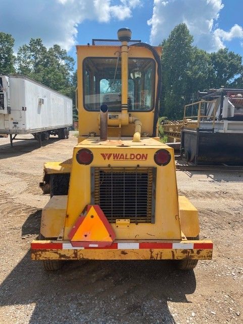 A yellow waldon truck is parked in a dirt lot
