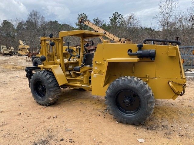 A yellow tractor is parked in a dirt field.