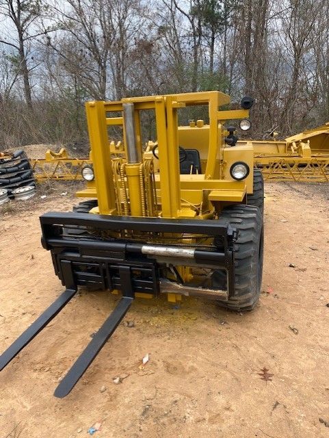 A yellow forklift with black forks is parked in the dirt