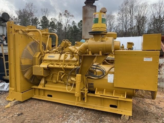 A large yellow generator is sitting on top of a dirt field.