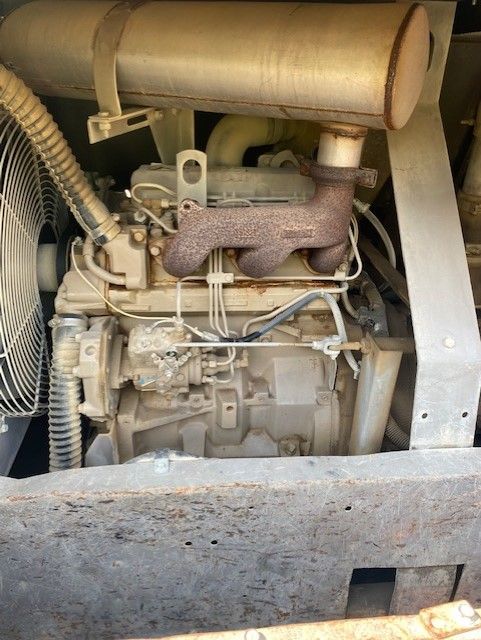 A close up of a dirty engine with a fan in the background