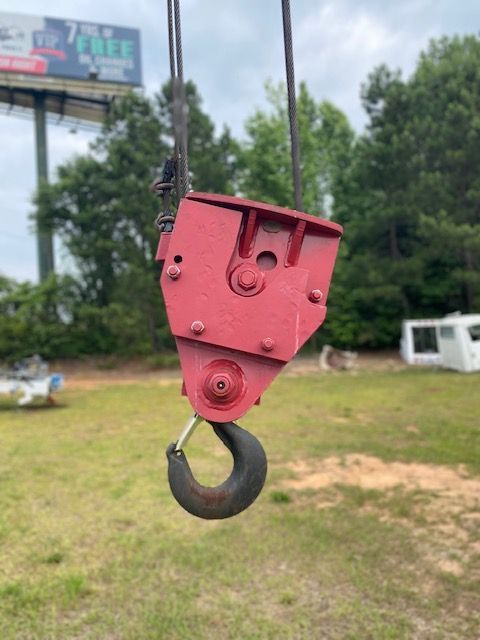 A red hook is hanging from a crane in a field.