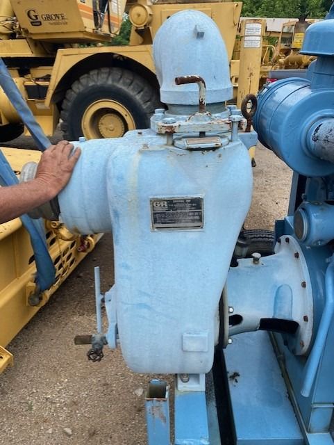 A man is touching a blue machine with a yellow truck in the background