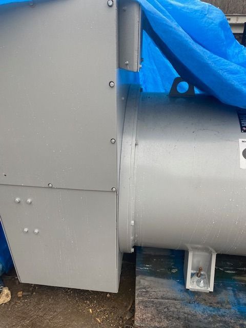 A large gray machine is sitting on top of a wooden pallet covered in a blue tarp.