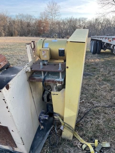 A yellow machine is sitting in a field next to a trailer.
