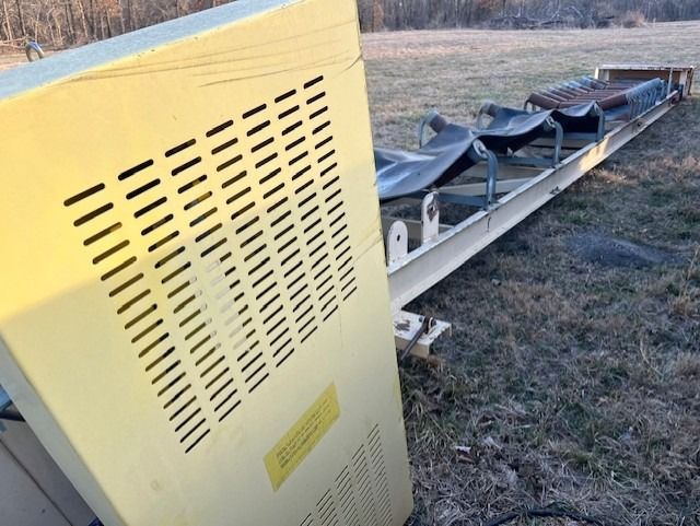 A conveyor belt is sitting in the grass next to a yellow box