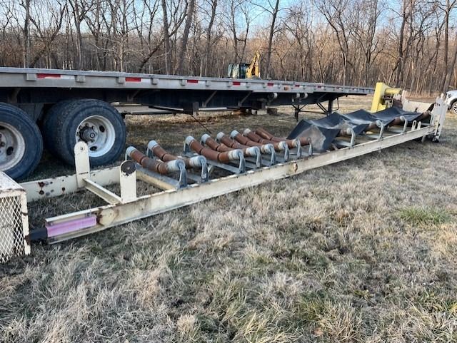 A conveyor belt is sitting on top of a trailer in a field.