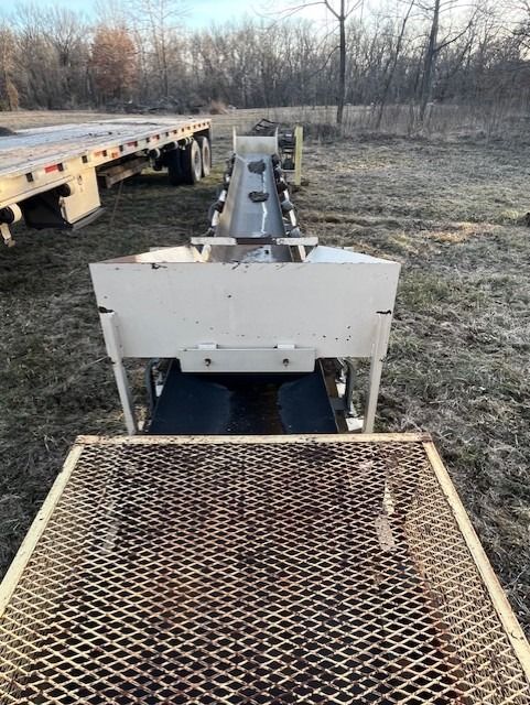 A conveyor belt is sitting on the ground next to a trailer.