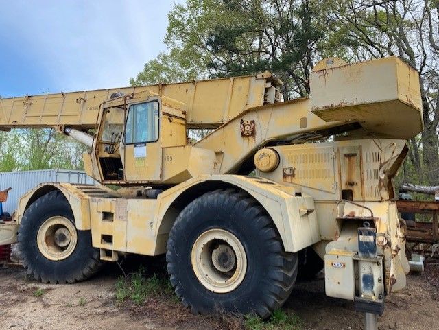 A large yellow crane is parked in the dirt in a field.